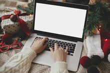 Hands working on laptop with blank screen on cozy bed with stylish christmas ornaments, present and santa hat. Christmas shopping online and freelance in holidays. Space for text