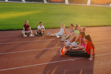 Wall Mural - A large group of children, boys and girls, sit and listen to the coach's instructions before the game at the stadium during sunset. A healthy lifestyle.