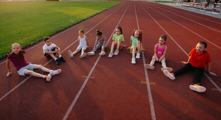 Wall Mural - A large group of children, boys and girls, sit and listen to the coach's instructions before the game at the stadium during sunset. A healthy lifestyle.