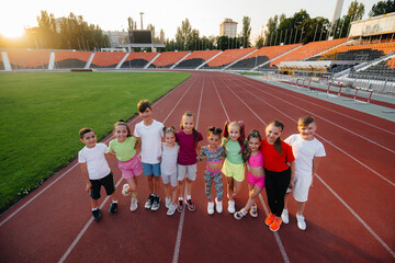 Wall Mural - A large group of children, boys and girls, rejoice together and wave their hands at the stadium during the sunset post game. A healthy lifestyle.