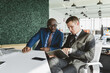 © xartproduction - Mature afroamerican businessman to discuss information with a younger colleague. People working and communicating while sitting at the office desk together with colleagues sitting.