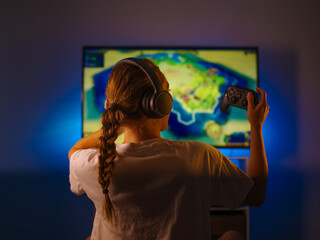 Poster - Gamer girl in headphones and with a joystick plays a video game. Close-up. Shooting from the back. Video games, strategy games, gambling business, rest, quarantine, relaxation.