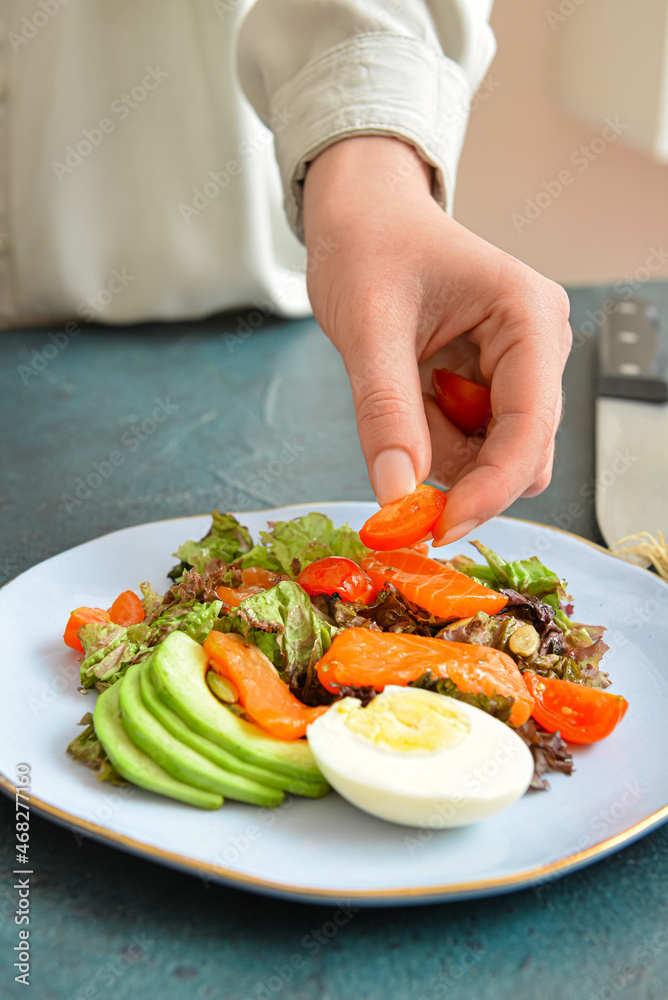Woman preparing fresh salad with salmon and vegetables at table, closeup
