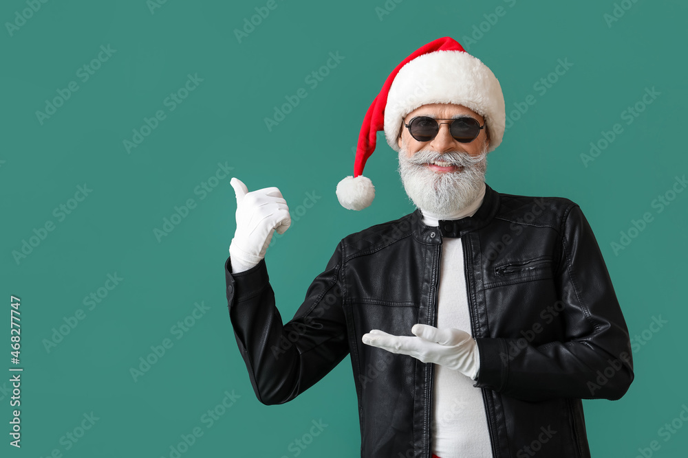 Cool Santa Claus in leather jacket pointing at something on color background