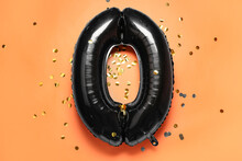 Black Balloon In Shape Of Figure 0 And Confetti On Orange Background