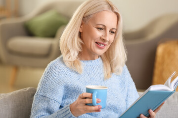 Wall Mural - Beautiful mature woman reading book and drinking tea at home