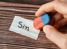 Sin And Grace Handwritten Words On Paper And Rubber Eraser In Woman's Hand On Wooden Table Background. Christian Biblical Concept Of Mercy And Salvation From God Jesus Christ. Top View. A Close-up.