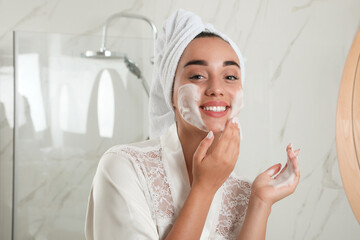 Poster - Beautiful young woman applying cleansing foam onto face in bathroom. Skin care cosmetic