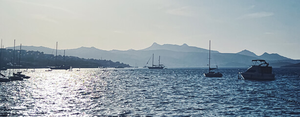 Wall Mural - Tranquil seascape and coastal nature concept. Sea, boats, mountains and blue sky over horizon at sunset.