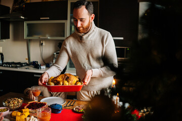 Side view of young man putting dish with grilled hot turkey on holiday dinner table served for Christmas family party, celebrating thanksgiving day with roasted turkey for dinner.