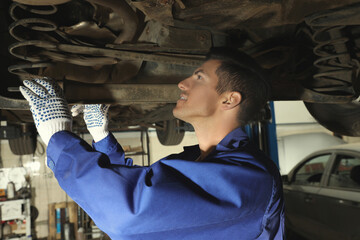 Poster - Professional mechanic fixing lifted car at automobile repair shop