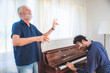 © chokniti - Mature and senior man with grey hair singing at home with eyes closed having young and handsome son play music and tune on piano