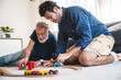 © chokniti - Closeup of a young man and elderly father playing with toy train set at home by sitting on floor in the living room and having fun and enjoying