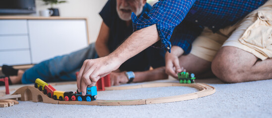 Closeup of a young man and elderly father playing with toy train set at home by sitting on floor in the living room and having fun and enjoying