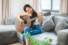 Asian Woman Playing Music By Guitar At Home, Young Female Guitarist Musician Lifestyle With Acoustic Art Instrument Sitting To Play And Sing A Song Making Sound In Hobby In The House Room