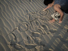 Child In Gray T-shirt And White Shorts Writing His Name From The Sand On The Beach