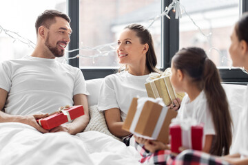 Sticker - family, winter holidays and people concept - happy mother, father and two daughters in pajamas with christmas gifts in bed at home