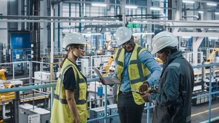 Leinwandbilder - Young Diverse Team of Car Factory Engineers in High Visibility Vests Using Laptop Computer. Automotive Industrial Manufacturing Facility Working on Vehicle Production. Diversity on Assembly Plant.