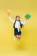 Happy schoolkid with backpack and notebooks jumping on yellow
