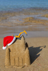 Wall Mural - model of orange toy excavator, Santa hat on the sand castle on the coast beach on a sunny day. The concept of Christmas business greetings, new year holidays in construction companies