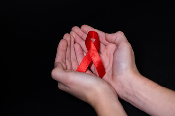 Child human hands hold red ribbon symbol of AIDS on a black background