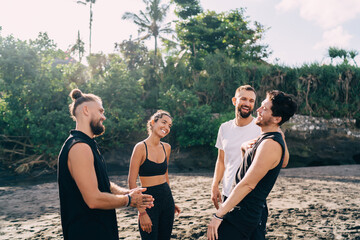 Group of cheerful male and female tourists laughing at seashore coastline spending daytime for together training at nature in Indonesia, happy best friends enjoying live communication at seashore