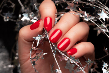 Wall Mural - Female hand with beautiful holiday manicure - red nails with silver Christmas twisted wire with stars. Selective focus. Closeup view. Nail care concept