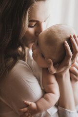 beautiful young mother holds newborn baby girl in white lighter room at home. tenderness cozy atmosp