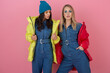 © mary_markevich - two attractive stylish women posing on pink background in colorful winter down jacket of red and yellow color, warm clothes fashion trend