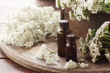 Yarrow Herb Essential Oil Or Extract In Amber Bottles With Milfoil Blossoms On Wooden Rustic Background, Closeup, Natural Cosmetics And Naturopathy Concept
