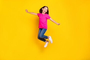 Wall Mural - Photo of funny positive girl jump carefree flight wear pink t-shirt jeans sneakers isolated yellow color background