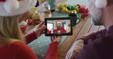Smiling Caucasian Couple With Santa Hats Using Tablet For Christmas Video Call With Woman On Screen
