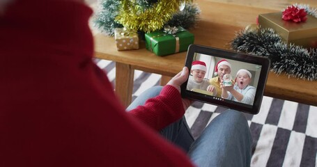 Canvas Print - Caucasian man waving and using tablet for christmas video call with smiling family on screen