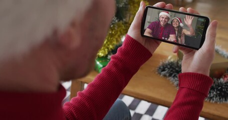 Canvas Print - Caucasian man with santa hat using smartphone for christmas video call with smiling couple on screen