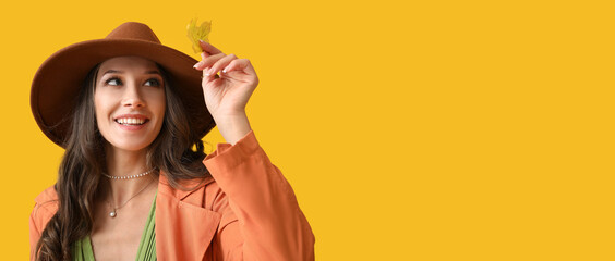 Wall Mural - Stylish young woman in autumn clothes and with leaf on color background with space for text