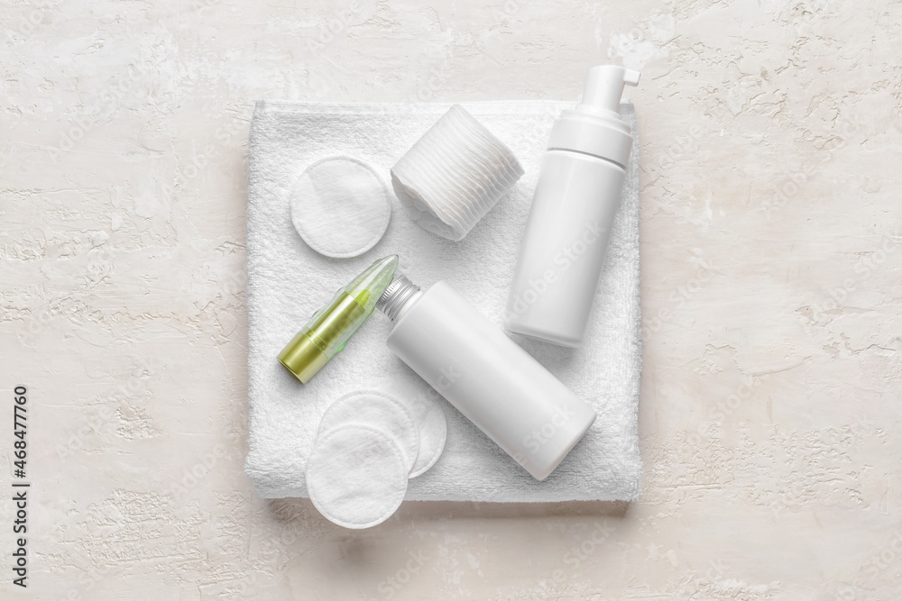 Cotton pads, care cosmetics and towel on light background