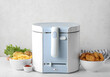 Deep fryer with bowls of delicious fast food and vegetables on table