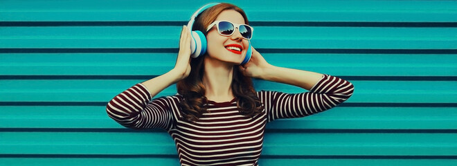 Wall Mural - Portrait of happy smiling young woman with headphones listening to music on a colorful blue background