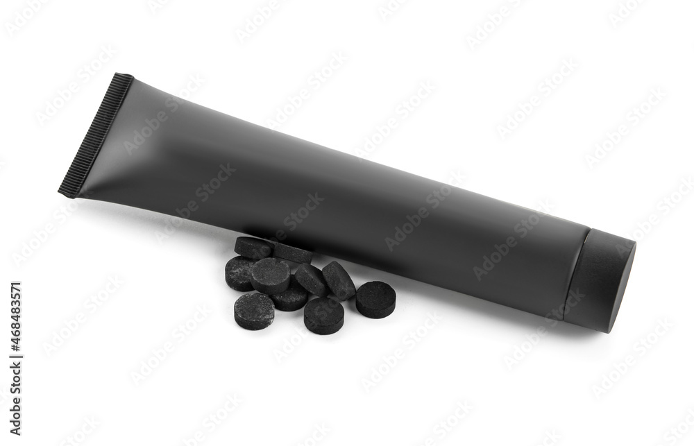 Tube of toothpaste with activated carbon and pills on white background