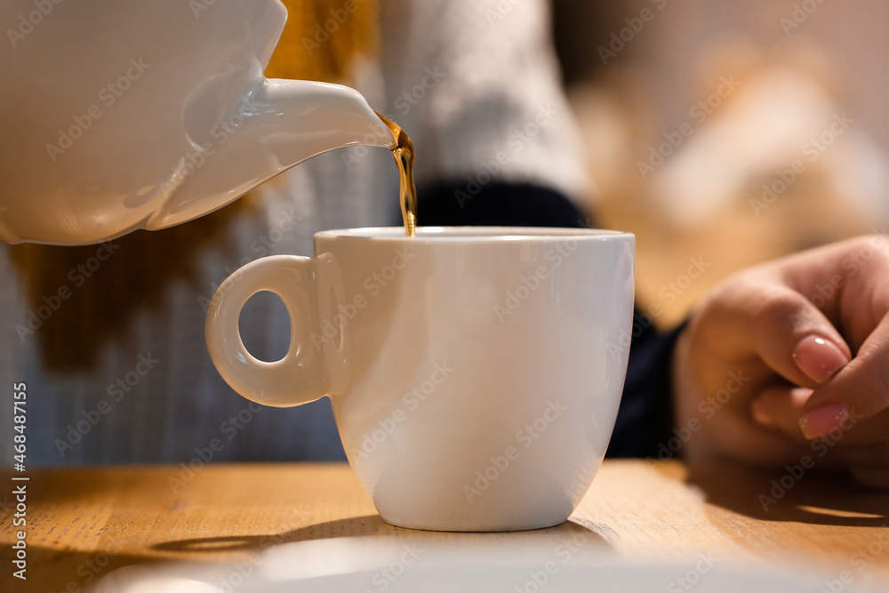 Woman pouring tea from pot into cup at table in cafe