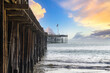 a stunning shot of a long winding brown wooden pier at the beach with vast blue ocean water and silky brown sand with blue sky and powerful clouds at Ventura Pier in Ventura California USA