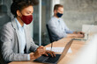 © Drazen - Black businesswoman wears face mask while working on laptop in office during coronavirus pandemic.