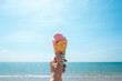 Strawberry ice cream in a wafer cone sticking out held in woman`s hand with tropical beach background. Summer concept