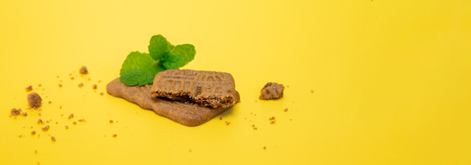 Wall Mural - two chocolate brown cookies decorated with mint leaves isolated over bright yellow background, studio shot. High quality photo