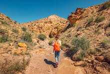 A Woman With A Backpack Walks Along A Trail In A Deserted Canyon With Red Rocks. Hiking Path And The Dangers Of Solo Trekking
