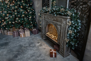 Wall Mural - Christmas luxury interior in a dark loft. The wooden fireplace is decorated with golden toys and a pine garland. Large Christmas tree with gifts wrapped in bright paper. Copy space