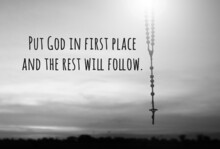 Faith Inspirational Quote - Put God In First Place And The Rest Will Follow. With Rosary And Jesus Christ Holy Cross Crucifix Hanging And Light On Sky Background In Monochrome Black And White.