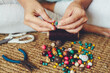 People at home with work or hobby job activity. Close up of woman hands making cheap jewelry to sell with wooden colorful beads and cords. Bracelet or necklace artisan production