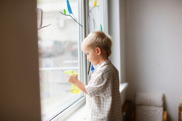 Cute boy toddler blond toddler at the window washes the glass. Helping children with household chores and household chores, children's independence, Montessori classes for small