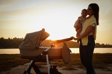 Canvas Print - Happy mother with baby walking near river at sunset